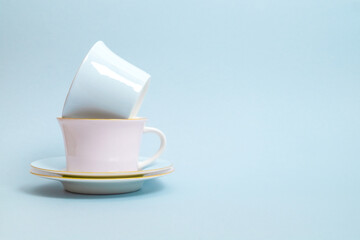 Two porcelain cups and saucers for tea or coffee in blue and pink colors stand on a blue background. Pastel colors. Selective focus. Copy space.