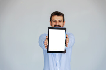 Smiling bearded businessman standing in front of white background and holding tablet. Selective focus on tablet.