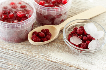 Frozen healthy cranberries in a plastic containers with cube of ice on wooden background