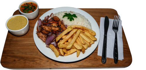 Peruvian food saltado chicken, french fries, seasoned chicken, onions, tomatoes, roasted vegetables, white rings on a white plate, together with cutlery and wooden background.