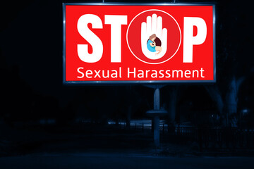 Advertising billboard with text STOP SEXUAL HARASSMENT at night outdoors