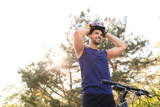 Male Cyclist Putting On Helmet Outdoors