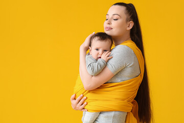 Young mother with little baby in sling on color background