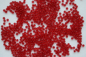 Red beads scattered on a white background. Materials for needlework.
