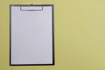 A black folder with a clip and attached white sheet on an isolated yellow background. Mockup for your text
