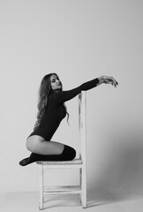 Young happy fitness girl with sporty body posing at studio on a blue background. Beautiful fit Girl. Fitness model in white sports bodysuit sitting on chair. Healthy lifestyle. Sexy woman.