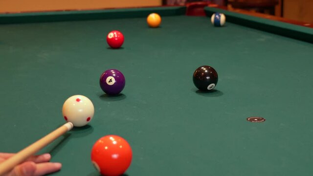 Person Playing Pool Shoots Purple Solid 4 Ball into Far Corner Pocket using Draw or Back Spin on the Cue Ball, closeup of Bridge Hand with Wooden Cue Stick Digging Into Green Felt or Cloth