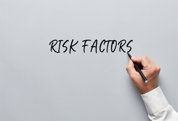 Businessman hand writing risk factors on gray background. Risk assessment or evaluation in business