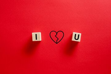 I love you word written on wooden cubes with a hand drawn broken heart shape against red background. Separation, divorce or breakup