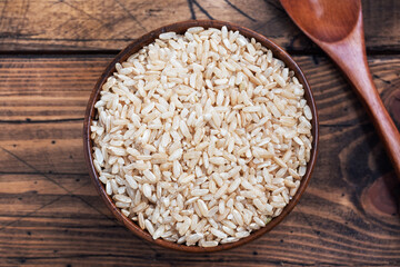 Brown rice raw long grain in a bowl, wooden background copy space, top view.