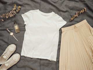 Fashionable female look with white empty t-shirt, cream pleated skirt and white sneakers. Top view...