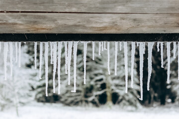 Icicles on the roof of the veranda of a wooden country house on the background of a beautiful winter landscape.family holidays during the Christmas holidays.Winter thaw