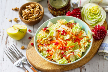 Dietary salad fresh vegetable of Chinese cabbage, carrots, apple, nuts and pomegranate with vinaigrette dressing on a white wooden table.