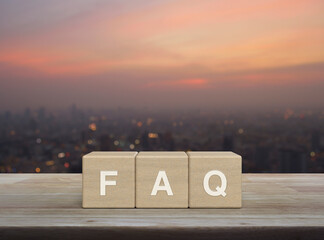 FAQ word on block cubes on wooden table over blur of cityscape on warm light sundown, Frequently...