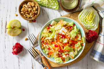 Dietary salad fresh vegetable of Chinese cabbage, carrots, apple, nuts and pomegranate with vinaigrette dressing on a white wooden table. Top view flat lay.