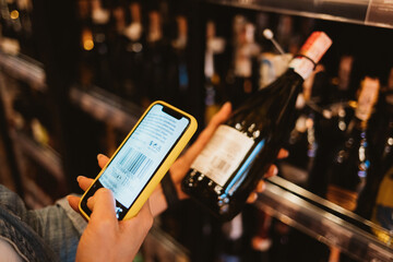 Woman customer scanning barcode from wine bottle label using smart phone