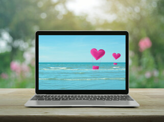 Pink fabric heart love air balloon on tropical sea with modern laptop computer screen on wooden table over blur flower and tree in garden, Business internet dating online, Valentines day concept