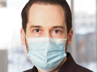 a man in a medical mask sits at the workplace in a chair in the office close-up portrait face