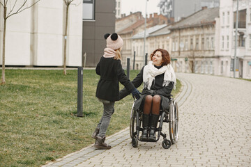 Disabled woman in wheelchair with daughter. Family walking outside at park.