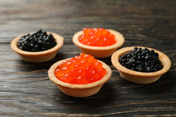 Tartlets with red and black caviar on wooden background, close up