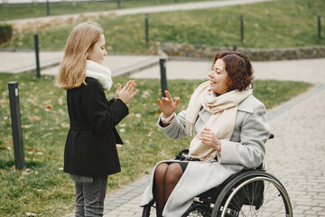 Fototapeta na wymiar Disabled woman in wheelchair with daughter. Family walking outside at park.