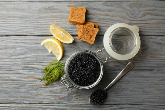 Jar with black caviar, bread, dill and lemon on wooden background, top view