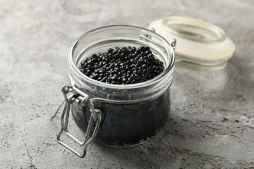 Fototapeta na wymiar Glass jar with black caviar on gray background