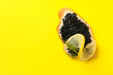 Delicious sandwich with black caviar on yellow background