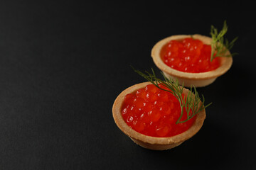 Tartlets with caviar on black background, space for text