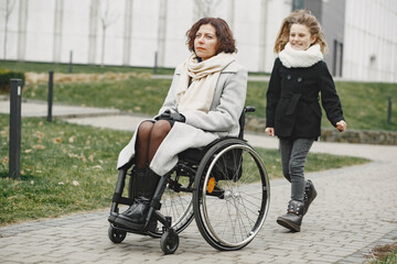 Fototapeta na wymiar Disabled woman in wheelchair with daughter. Family walking outside at park.