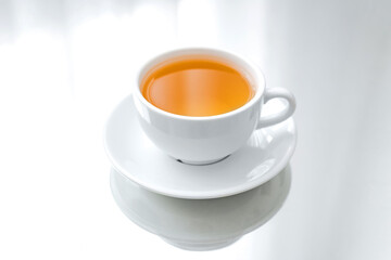 A horizontal photo of a white porcelain cup of green tea on a saucer, on a mirror table, a reflection