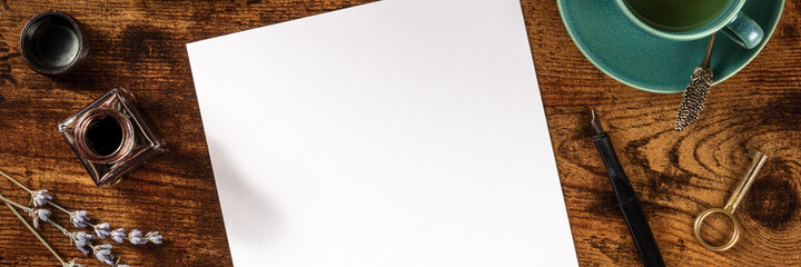Stationery panorama with copy space, ink, with a cup of tea, shot from above on a dark rustic wooden background
