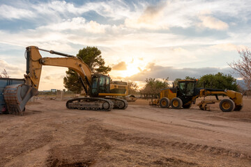 An excavator and motor grader parked on a construction site at sunset