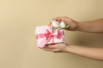 Female hands hold gift box with roses on beige background