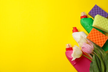 Detergents, sponges and tulips on yellow background
