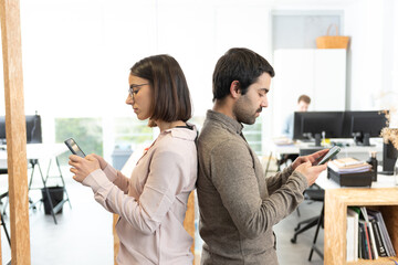 Female and male hispanic coworkers concentrated on their cell phones at the office.
