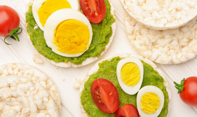 Close up rice cakes with avocado mash and eggs with tomato on with wooden background top view
