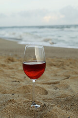 Glass of red wine on sandy sea beach