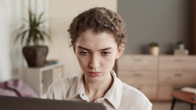 Medium close-up of young big-eyed Caucasian woman looking at invisible computer in front of her, then getting disappointed and sad, standing up and walking away