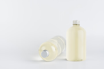 Set of two transparent plastic low thick bottles standing and lying with pale fresh drink or cosmetic essential oil and silver cap, mockup on white background,  front and side view.