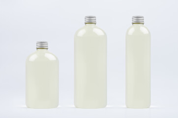 Assortment of three plastic tall, low and thick bottles with pale fresh drink or cosmetic essential oil, silver cap mockup on white background, template.