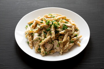 Homemade Chicken Alfredo Penne with Parsley on a black surface, side view.