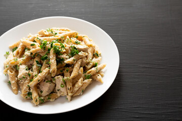 Homemade Chicken Alfredo Penne with Parsley on a black surface, side view. Copy space.