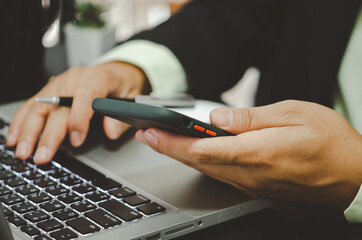 hand business man holding a mobile phone and typing on a computer keyboard.