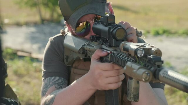 Closeup of brutal military man in sunglasses taking aim with rifle, looking at day scope