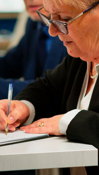 Busiess partners discussing new project for company evolution, senior manager woman checking tasks on clipboard and signing new contract. Executive director meeting shareholders in start up office