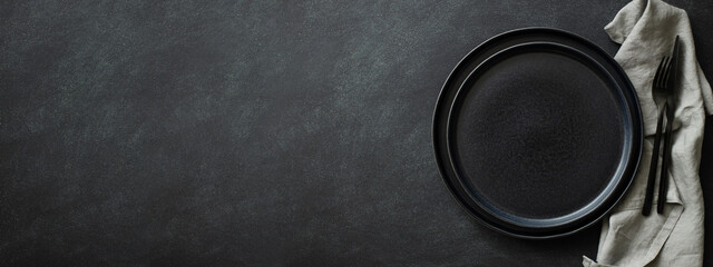 Empty black plates with black cutlery and gray napkin on black table. Top view, banner for website.