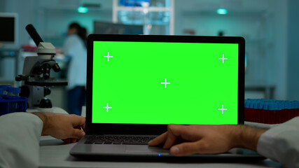 Pov shot of man scientist sitting at desk working on laptop with mock-up green screen, isolated...