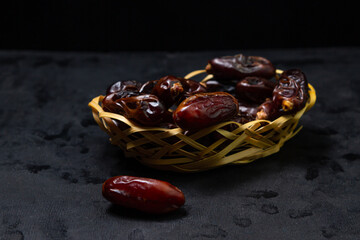 Dates on a black background. Dried fruits. Dried dates are in a small basket