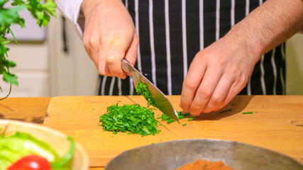 Chef chopping parsley with knife on a wooden board